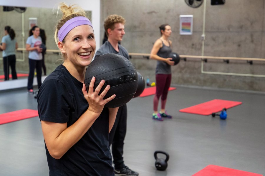 An Active Living Centre member smiles at the camera while holding a medicine ball during a group fitness class.