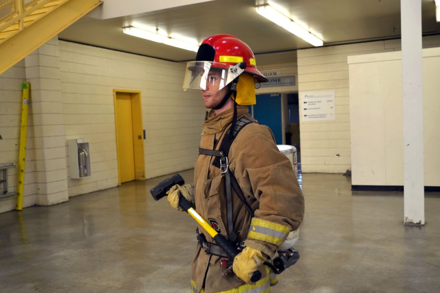 A fireman walks across a room in full gear carrying an axe.