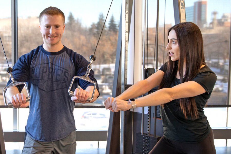 A personal trainer demonstrates to a trainee the proper technique for using a piece of resistance equipment. 