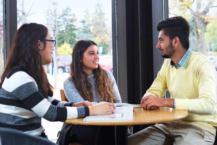 Three students sitting together and talking at a small round table.