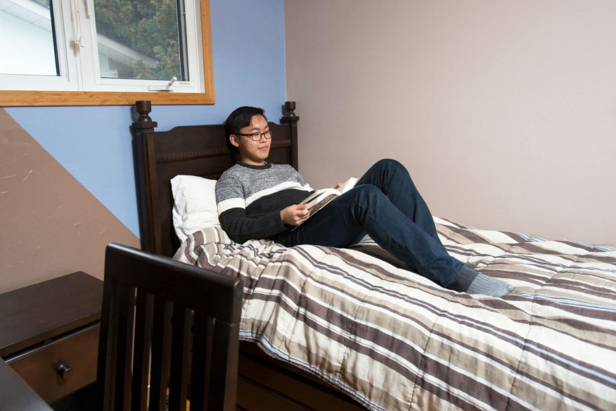 A student sits on a bed and reads in his homestay room.