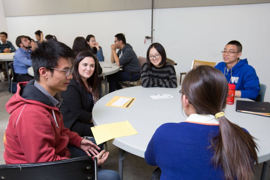 A classroom of students sitting around circular tables working. 