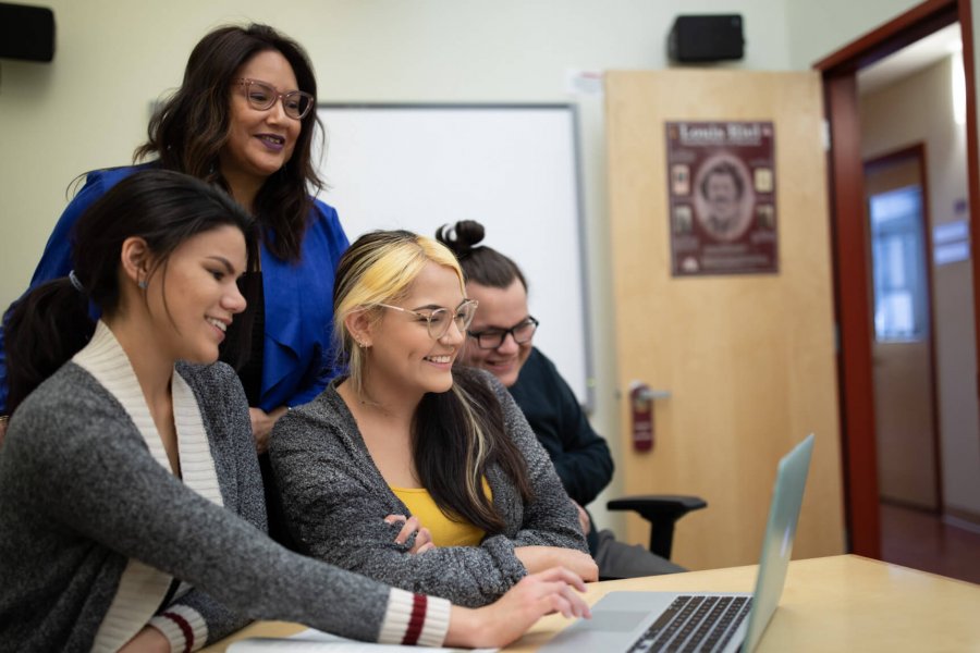 Three smiling students gather around a laptop with Indigenous Student Advisor Carla Loewen.
