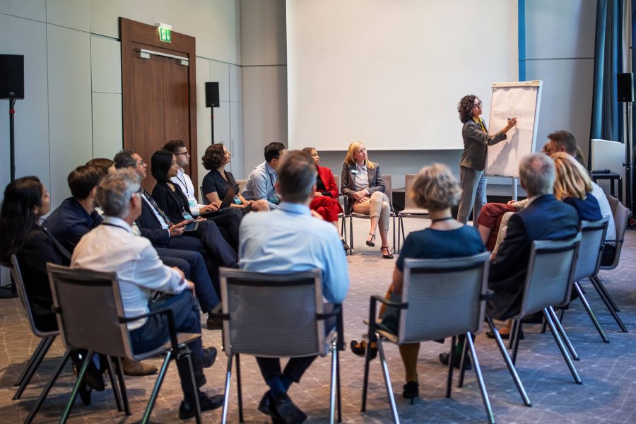 A group of adult learners seated in a circle while a standing person gives a presentation. 