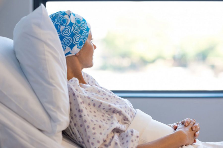 A cancer patient rests on a bed and looks out a window.