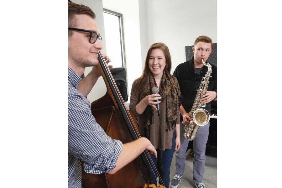 Three students practice their instruments together in a small practice room. 