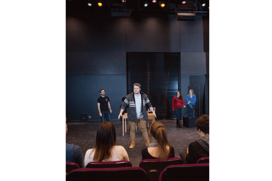 A small group of students performs on stage for an audience seated in a theatre.