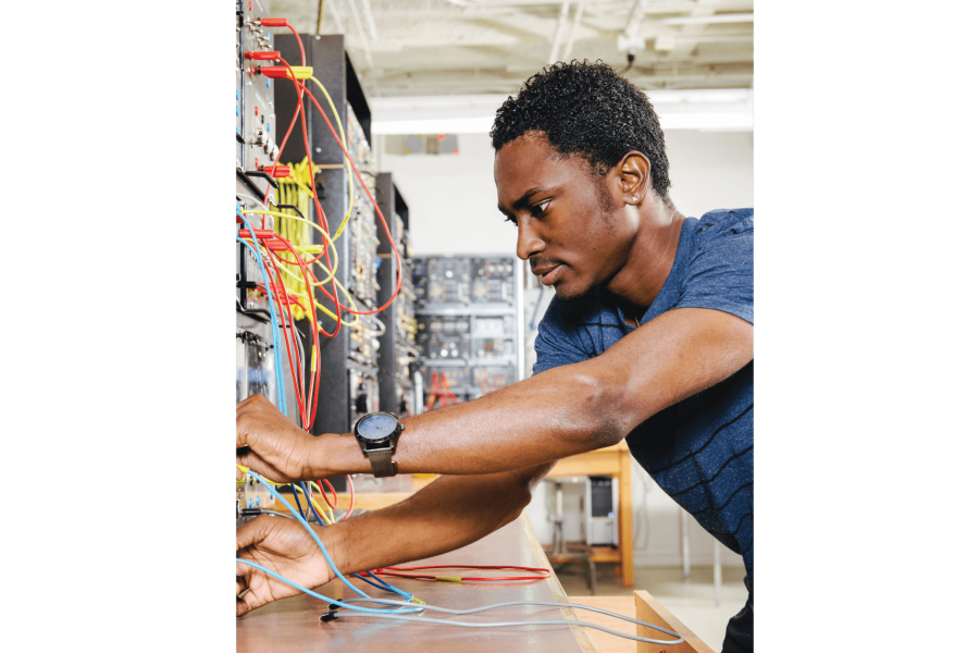 A student works at a desk connecting wires to a console. 