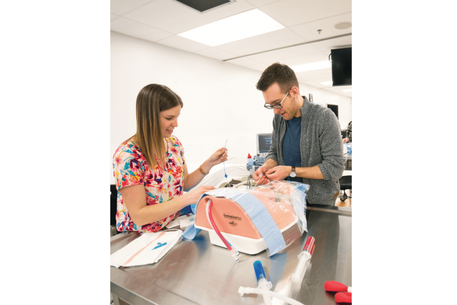 Two students practice setting an intravenous line on a mannequin. 