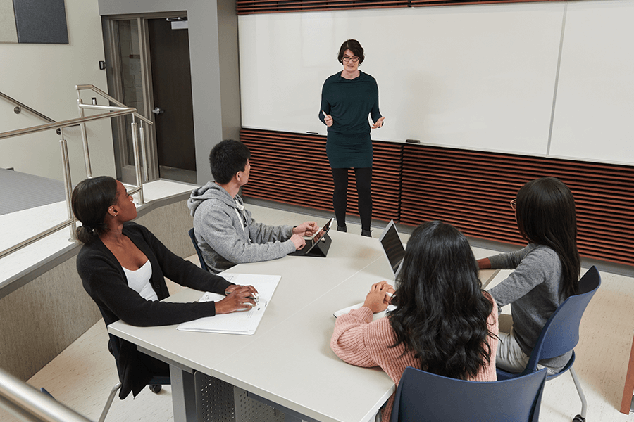 A professor speaking in front of a group of four students.