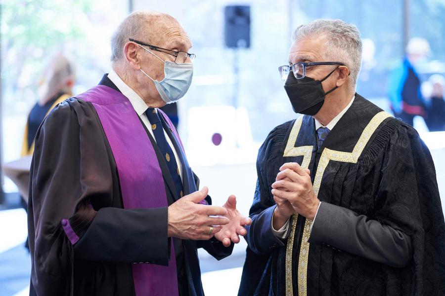 President Benarroch speaking with former president Arnold Naimark, wearing academic gowns and covid masks.