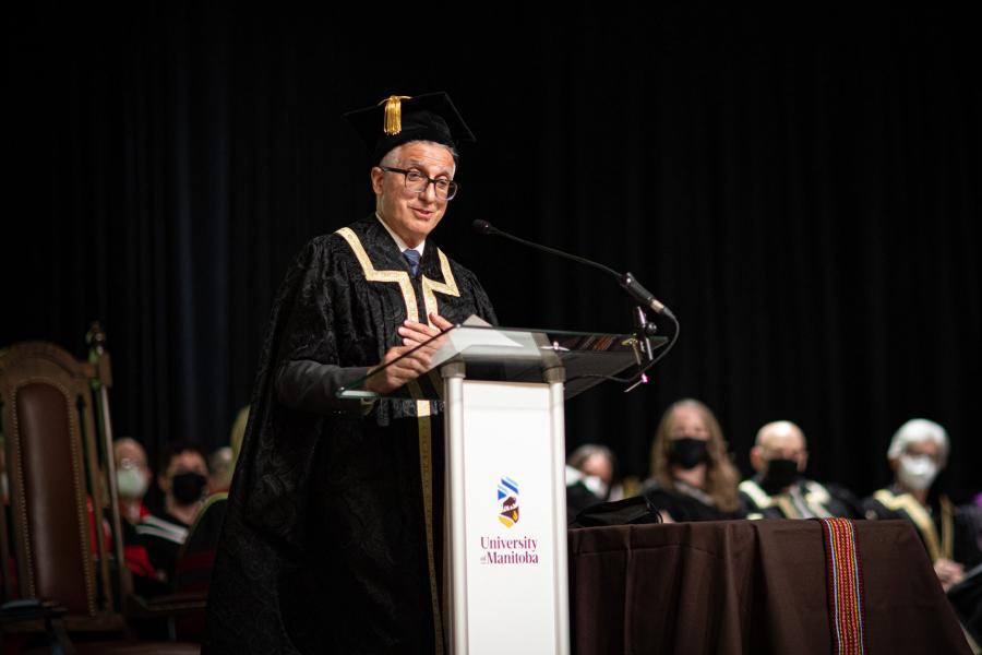 President Benarroch stands at a podium with the U M logo giving an address.