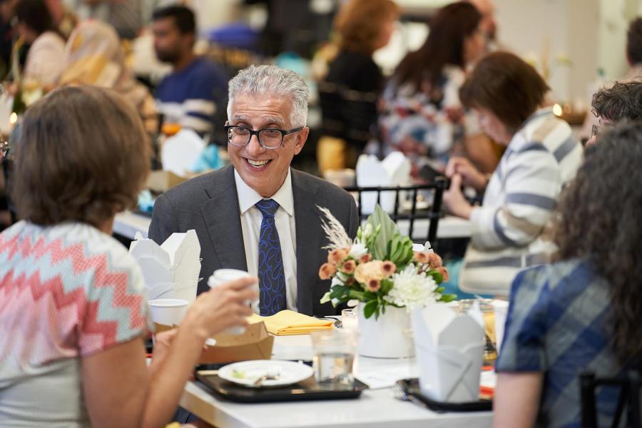 President Benarroch smiles, sitting at a lunch table with a floral centrepiece.