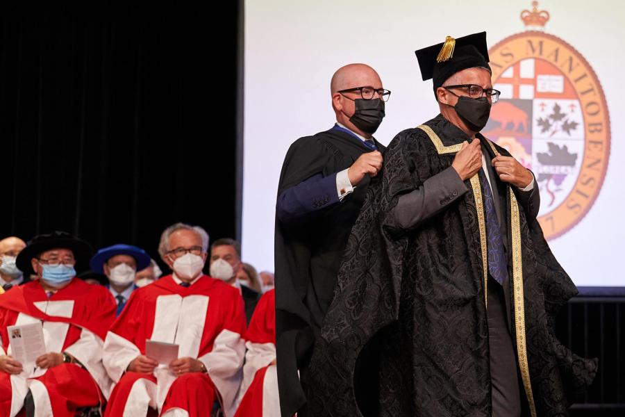 President Benarroch stands as a man behind him drapes black robes over his shoulders.