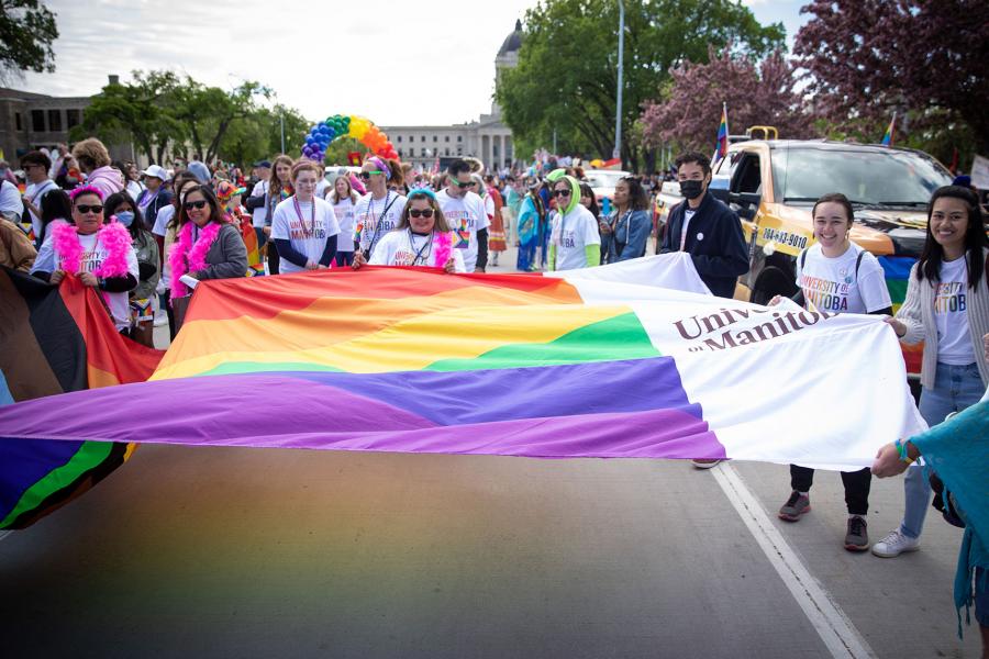 People hold a large UM Pride flag on Memorial Avenue in Winnipeg. Photo from the Winnipeg Pride Parade 2022.