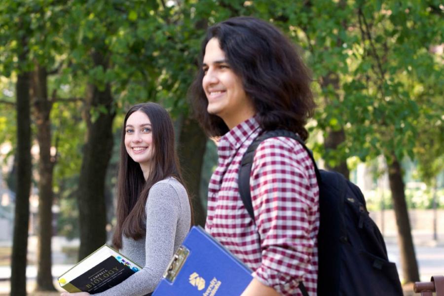 Two students walking outside carrying text books on Fort Garry campus.