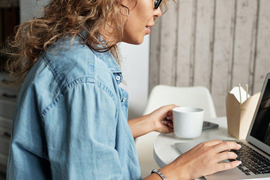 Woman working on a laptop with a cup of coffee in hand.