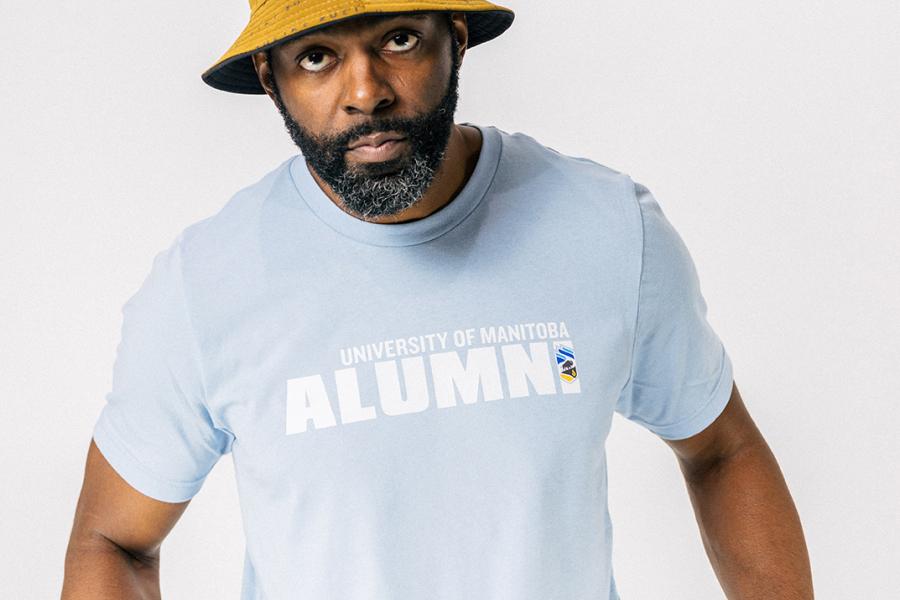 A male model wearing a light blue UM alumni tshirt and yellow bucket hat.