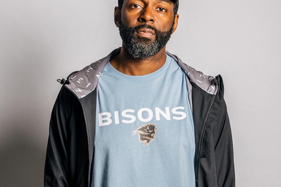 A male model wearing a light blue UM Bisons tshirt and black baseball hat.