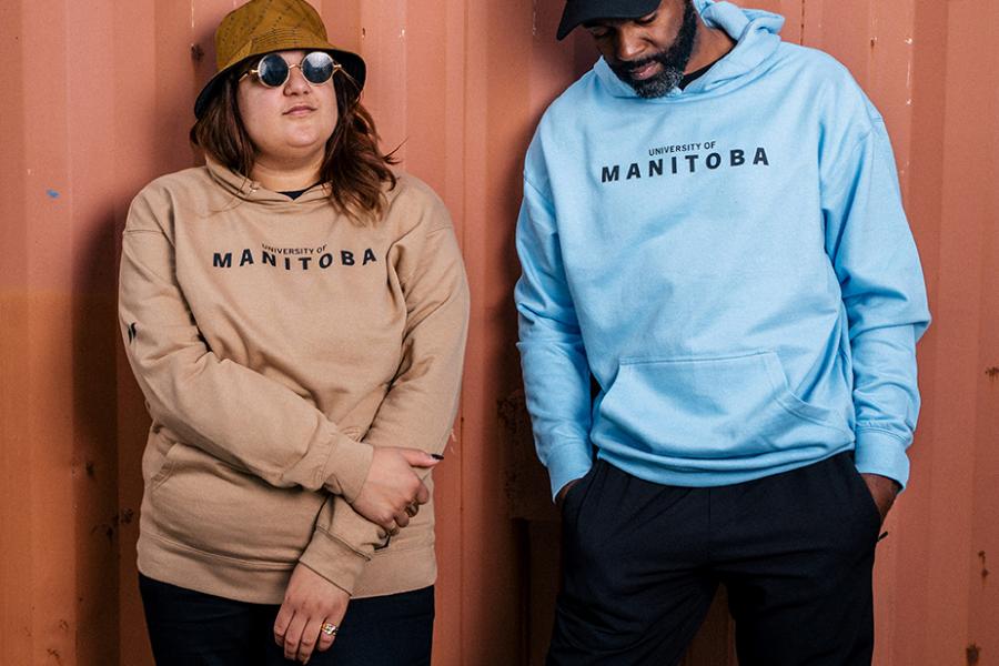 A male and female model wearing UM yellow and blue hoodies and hats.
