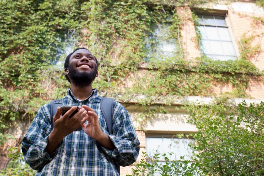 A University of Manitoba student smiles in front of an ivy-covered building.