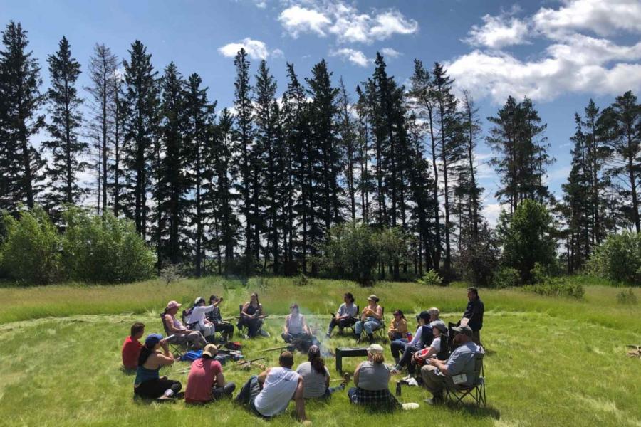 LAND AND WATER PARTICIPANTS GATHER WITH ELDERS AROUND A FIRE ON THE TWO-SPIRIT SUNDANCE GROUNDS.
