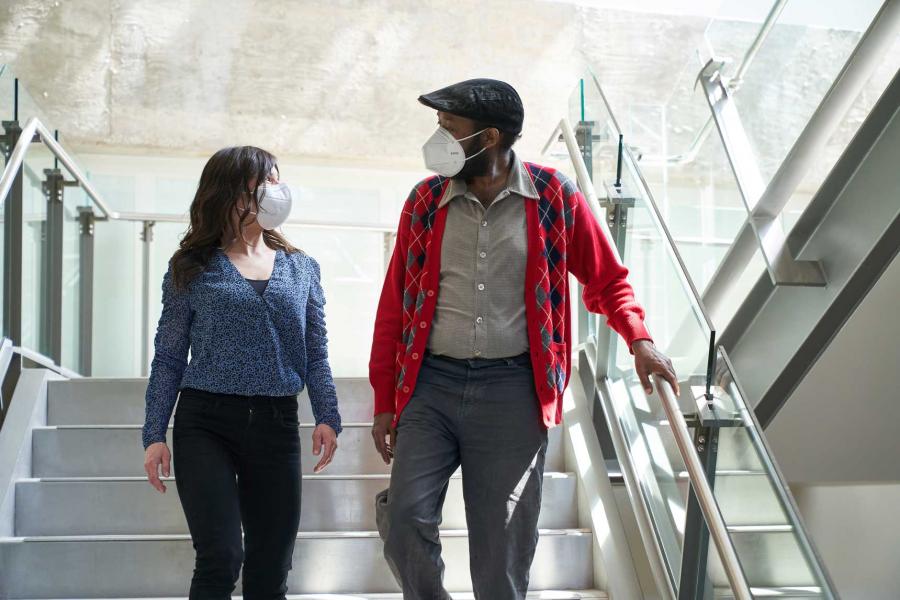 Two people wearing covid masks walk down a brightly lit set of stairs.