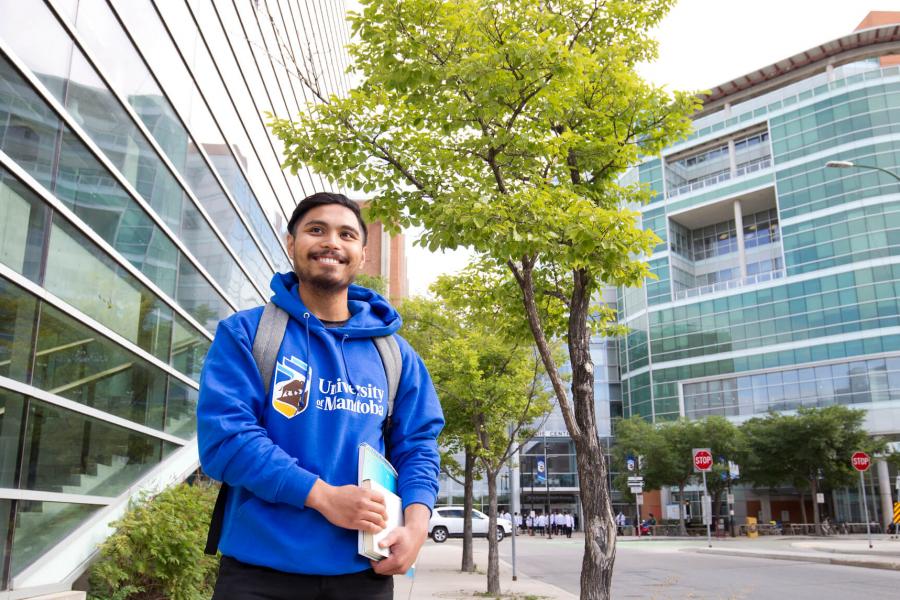 An image of a student smiling during a day summer standing by a green tree on UM's Bannatyne Campus.