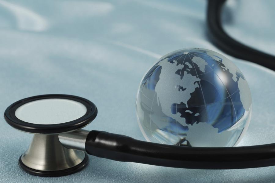 Close up of a stethoscope resting on a surface, a small globe is next to the stethoscope.