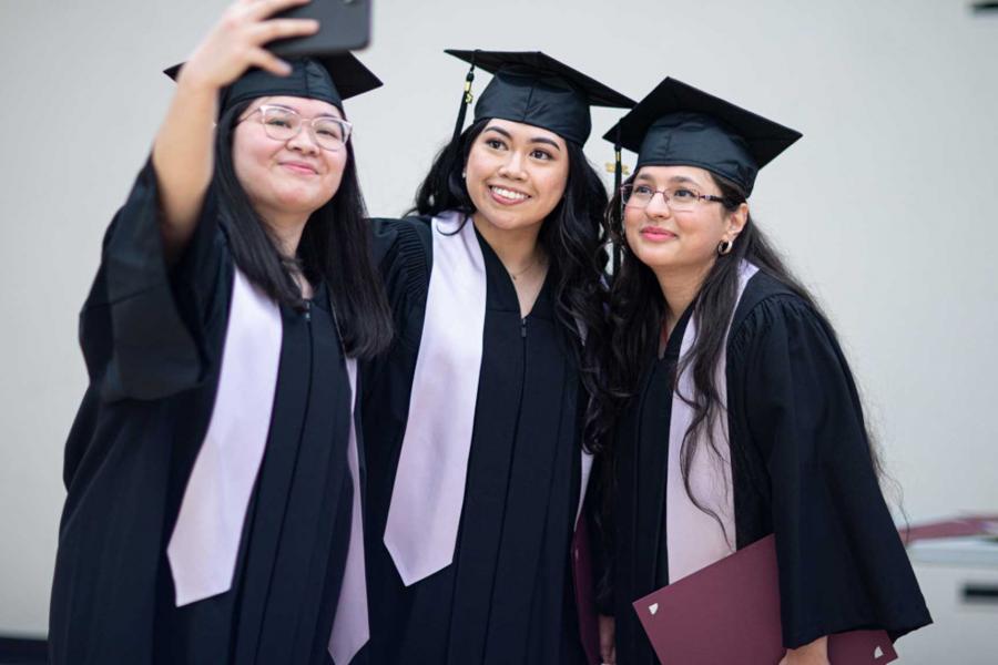 Three students in their cap and gowns at convocation taking a selfie.