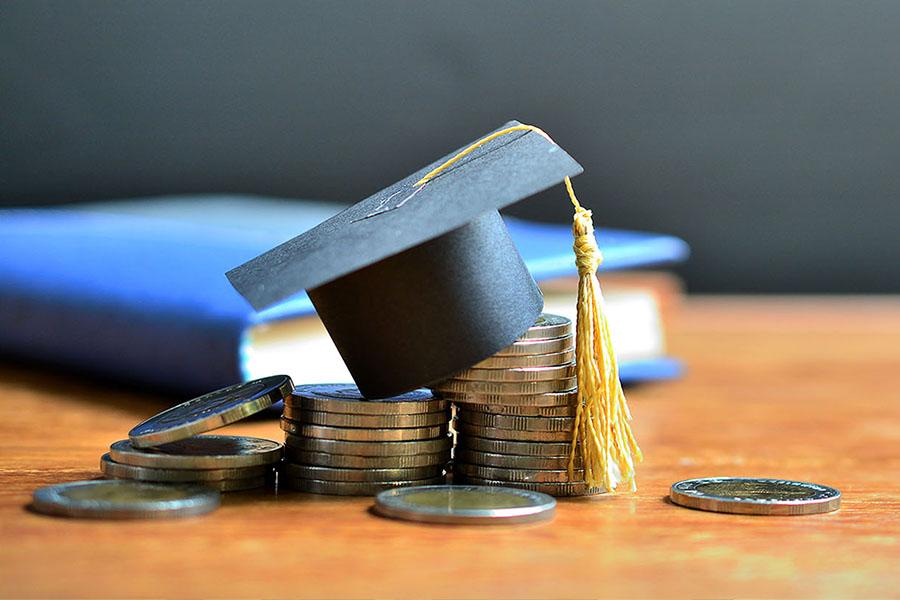 A table with a book and coins with a tiny graduation cap sitting on the coins.