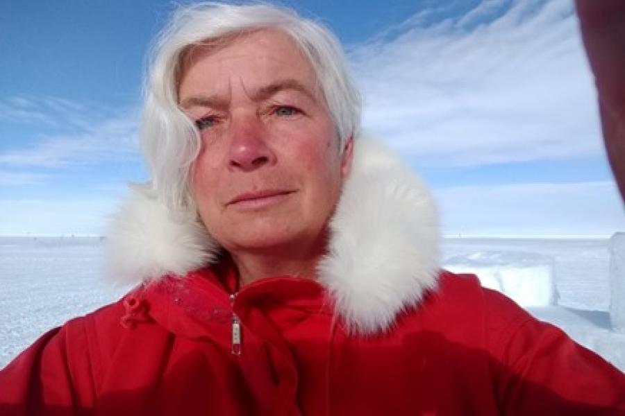  UM professor Dorthe Dahl-Jensen standing outside in Greenland in a red parka with white snow and blue sky in the background.