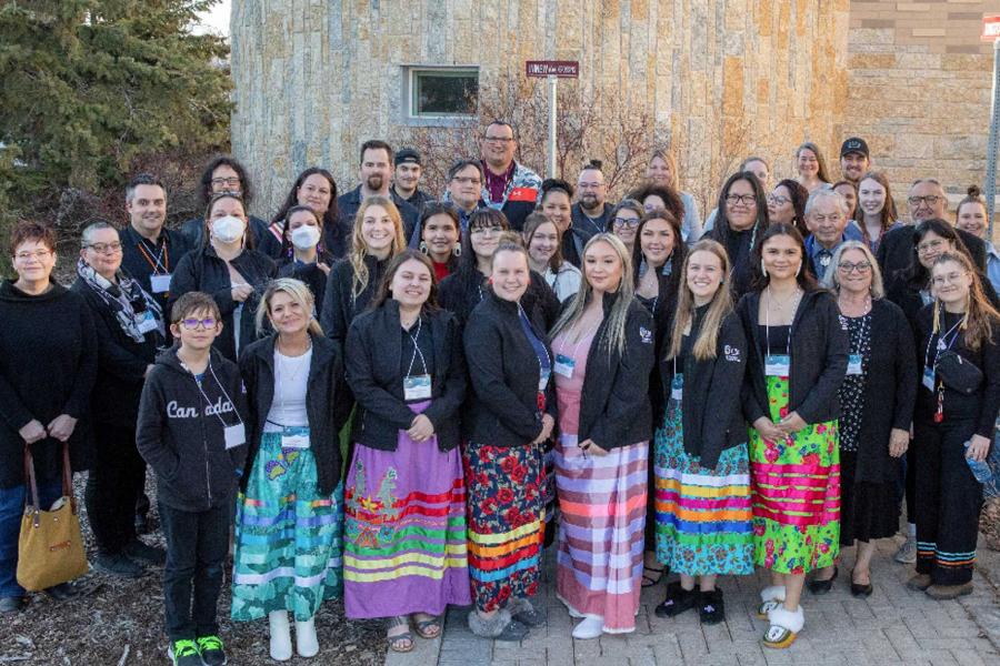 A group photo of participants – some wearing ribbon skirts – in the 2022-2023 ICE program with elders, ICE alum, community leaders and loved ones.