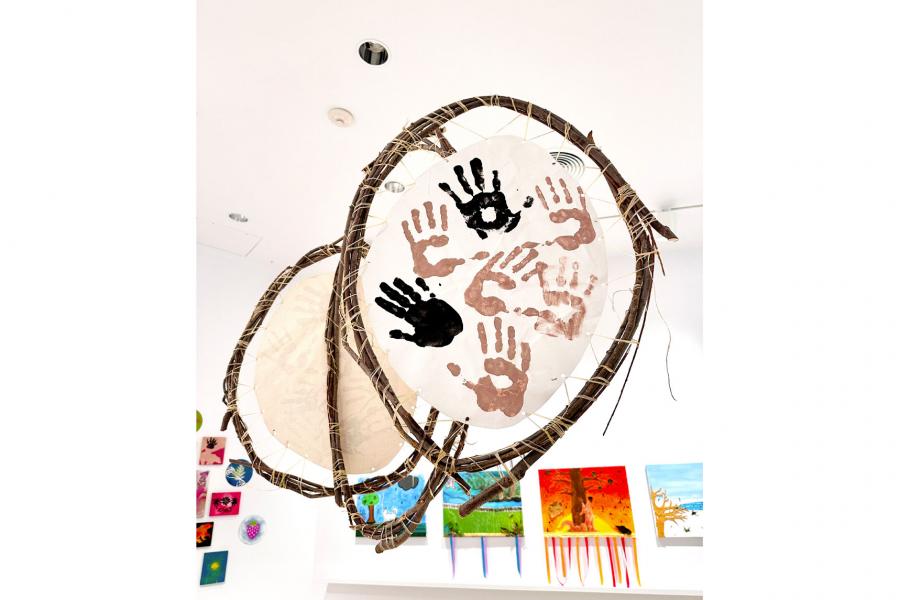 Willow branches, wrapped and tied together to form a circle, stretching animal hide with paint handprints on it.