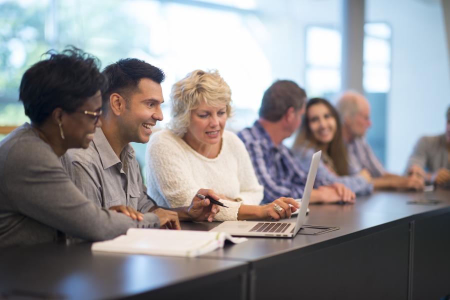 Group of adult learners in a classroom setting on laptops.