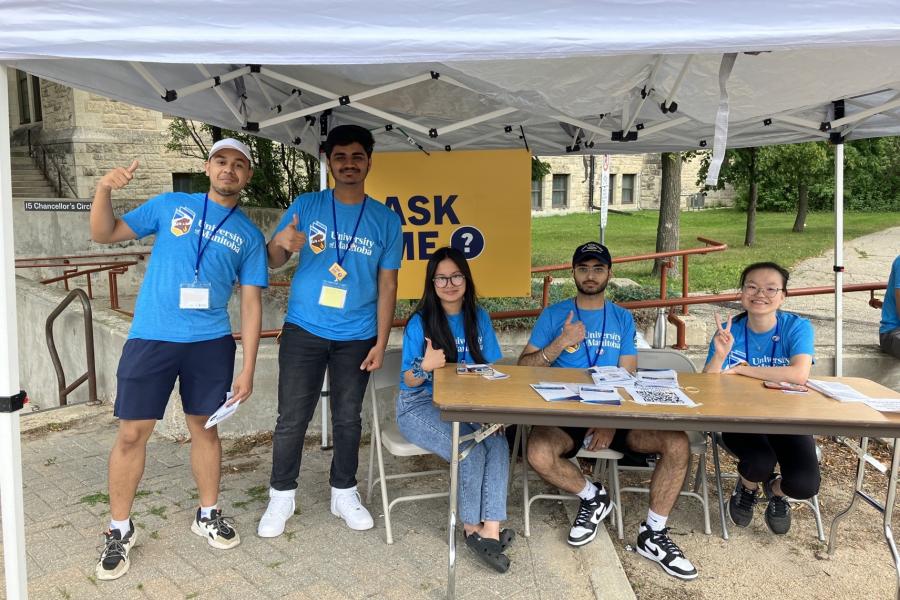 Volunteers wearing blue shirts working at the 'Ask Me' table during Orientation 2023