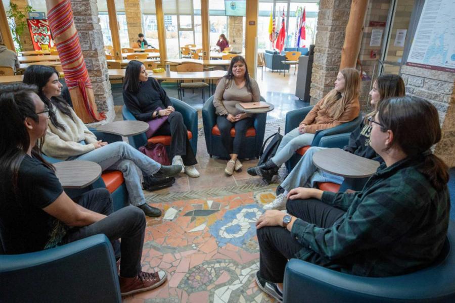 Seven Indigenous students seated in a circle having a conversation at Migizii Agamik. 