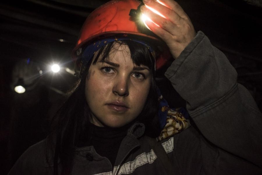 Image of artist Yevgenia Belorusets' "Victories of the Defeated" photograph featuring a woman in the dark wearing a red hard hat with a headlamp. She is covering the headlamp with her hand. 