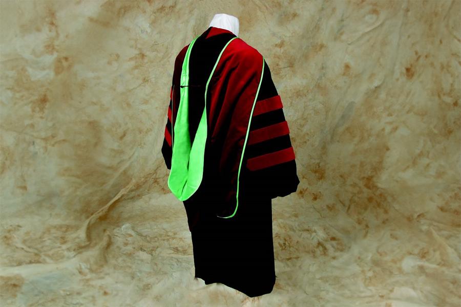 A mannequin wearing a red and black PhD graduation gown, there is a red velvet panel  the neck and the front, and the three red velvet bands on the bell-shaped sleeves. The hood is green.