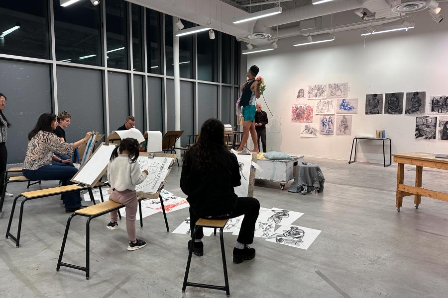 5 diverse people sketching a model who is posed an elevated box in a room with several sketches of people on the wall