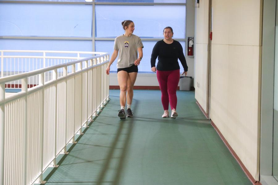 Two women walking on an indoor track.