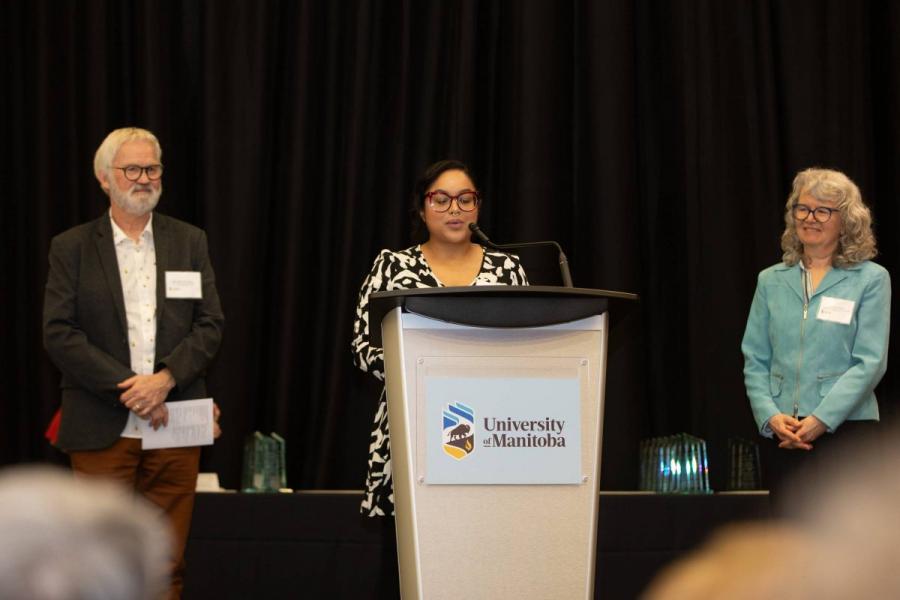 student award recipient at podium, with two teachers beside her