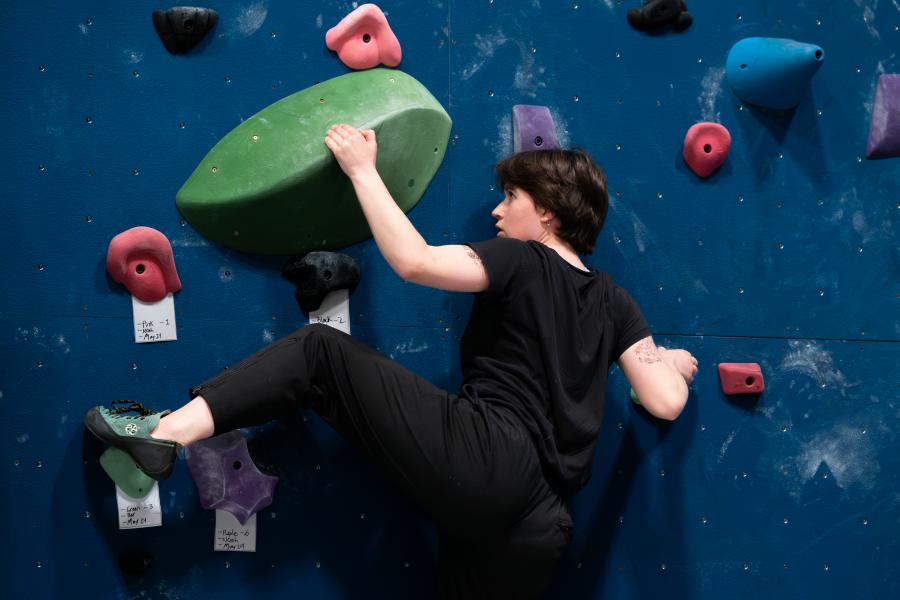 A climber holding onto a green rock on the bouldering wall