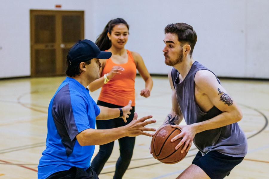 a person in a grey shirt holding a basketball facing off against a person in a blue shirt and hat