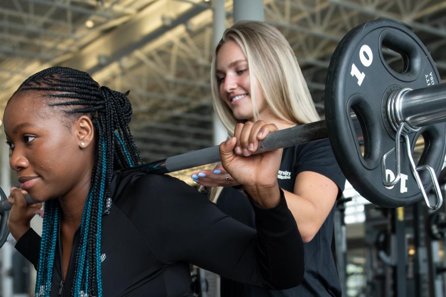 A personal trainer guides a client during a squat