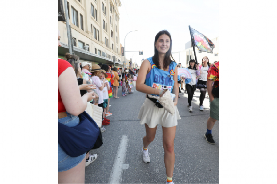 girl walking in Pride parade, handing out items to crowd