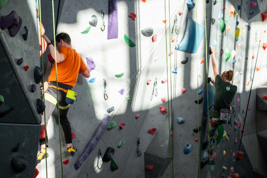 A person in an orange t-shirt climbing the UM climbing wall