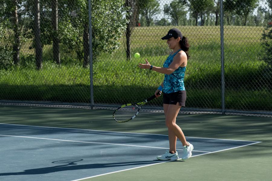 A woman in tennis gear smiles as she tosses the ball in the air