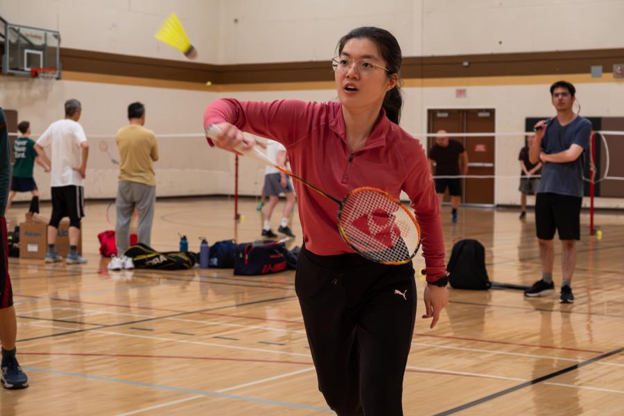 A woman in a red shirt swatting at a birdie with a badminton racket