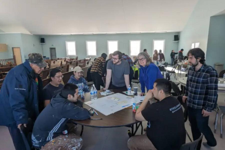 The interior of Wikiwin Training Enterprise at York Factory First Nation. People are surrounding a table looking at papers.